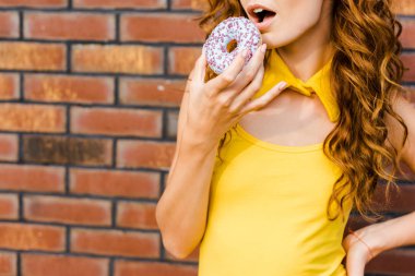 sarı giysili tuğla duvar önünde donut yemek çekici genç kadın görüntüsünü kırpılmış