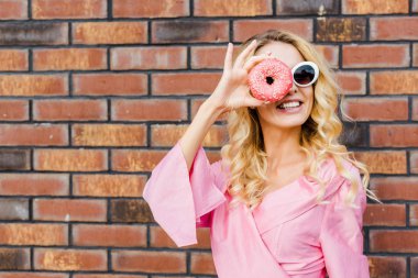 pembe gömlekli çörek tuğla duvar önünde kameradan bakarak mutlu genç kadın