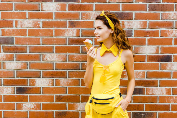 beautiful smiling woman in yellow clothes with ice cream posing in front of brick wall