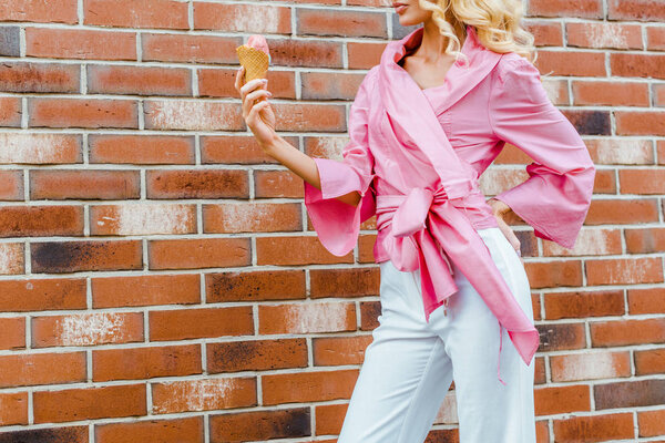 cropped shot of young woman in pink holding ice cream in front of brick wall