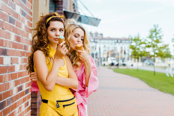 stylish young women in colorful clothes eating ice cream on street