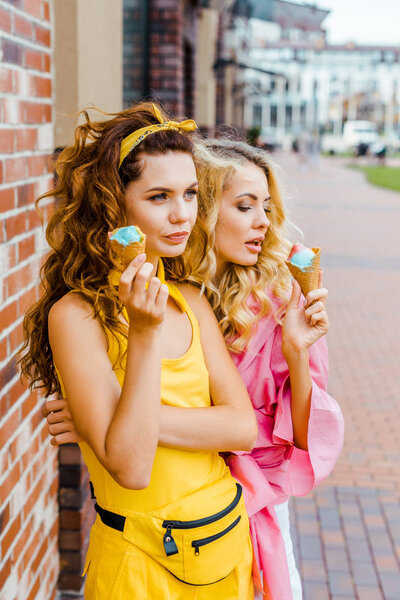 beautiful young women in colorful clothes eating delicious ice cream on street
