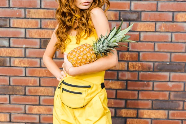 Beskuren Bild Ung Kvinna Gula Kläder Håller Ananas Framför Tegelvägg — Stockfoto