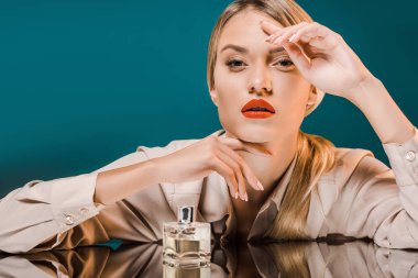 portrait of stylish blond woman leaning on mirror surface with perfume on dark background clipart