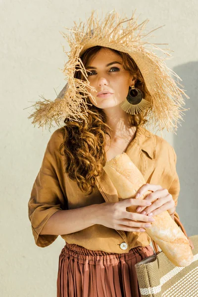 时尚美丽的女人在草帽与面包站在白色的墙前 — 免费的图库照片