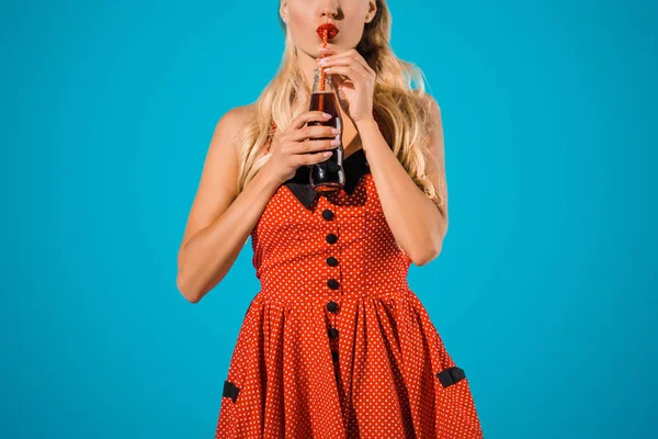 裁剪拍摄的别针女人在老式的礼服喝苏打饮料从孤立的玻璃瓶蓝色 — 图库照片