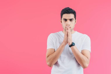 handsome man with hands in namaste gesture looking away isolated on pink clipart