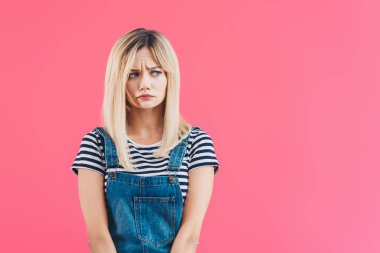 worried beautiful girl in denim overall looking away isolated on pink clipart
