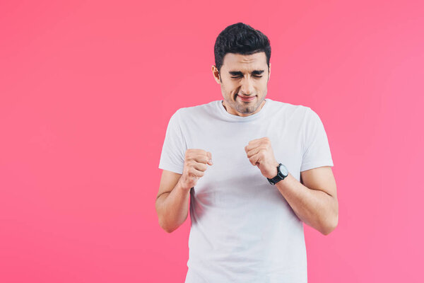 испуганный красивый мужчина с закрытыми глазами, стоящий с кулаками, изолированными на розовый
