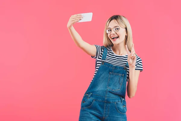 ピンクの分離のスマート フォン Selfie をしながらピースサインを見せて女性の肖像  — 無料ストックフォト