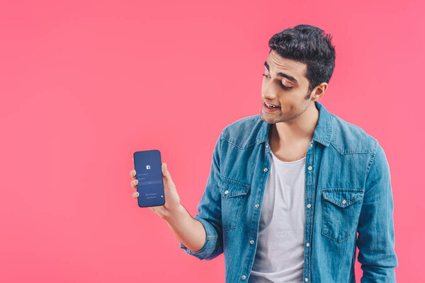 young man showing smartphone with facebook website isolated on pink