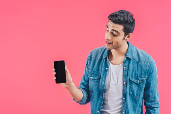 smiling young man showing smartphone with blank screen isolated on pink