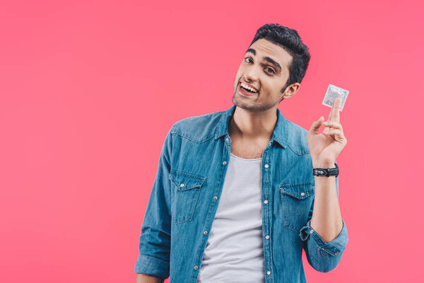 happy young man showing condom isolated on pink