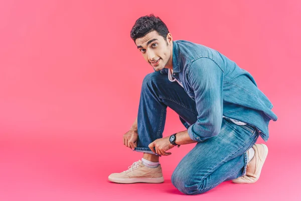 Joven Elegante Hombre Sentado Ajustando Pantalones Vaqueros Aislados Rosa — Foto de Stock