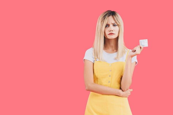 emotional young stylish woman holding condom isolated on pink