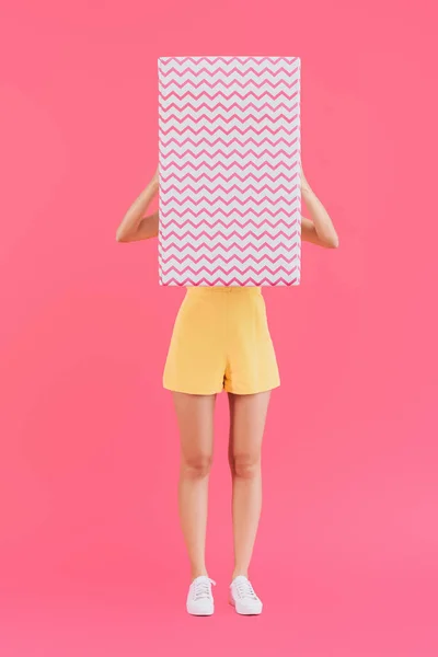 ピンクの分離した大きなギフト ボックスで顔を覆っている若い女性  — 無料ストックフォト
