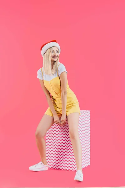 Attraktive Lächelnde Junge Frau Mit Weihnachtsmütze Sitzt Auf Großer Geschenkbox — kostenloses Stockfoto