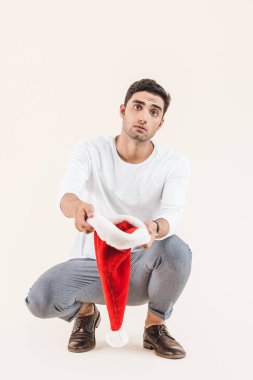 young man holding santa hat and begging isolated on beige clipart