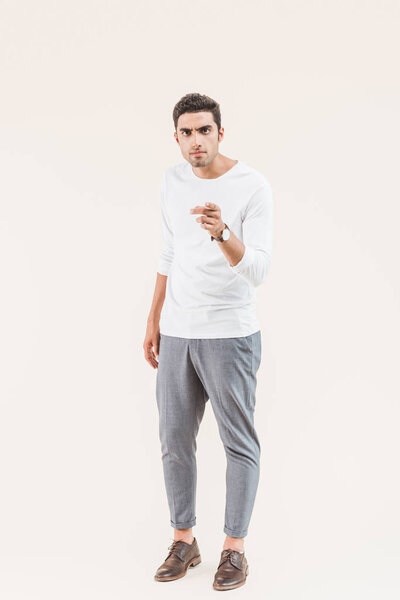serious young man looking at camera and pointing with finger isolated on beige