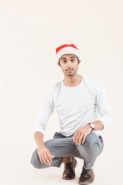 Geschokt Jongeman Kerstmuts Crouching Kijken Naar Camera Geïsoleerd Beige — Gratis stockfoto