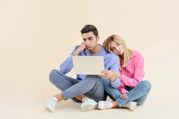 Bored Young Couple Sitting Together Using Laptop Isolated Beige — Stock Photo, Image