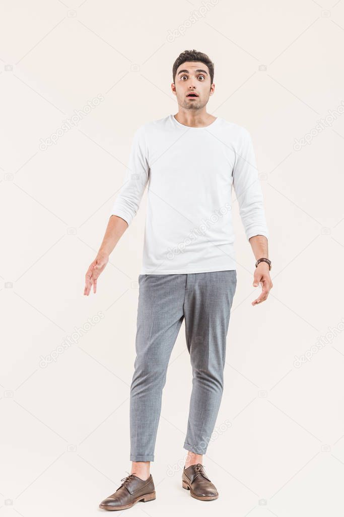full length view of shocked young man looking at camera isolated on beige