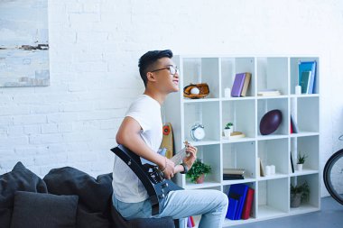 yan görünüm gülümseyen yakışıklı Asya adam oynayan elektro gitar evde unplugged