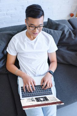 Asya yakışıklı yüklü bbc Haberler sayfasında evde kanepe ile dizüstü bilgisayar kullanarak görünümünü yüksek açı