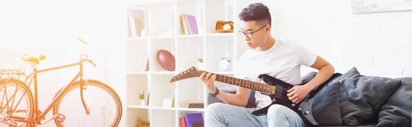 Panoramik Yakışıklı Solak Asya Adam Evde Kanepede Elektro Gitar Çalmak — Stok fotoğraf