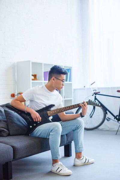 handsome asian man playing F major chord on unplugged electric guitar at home