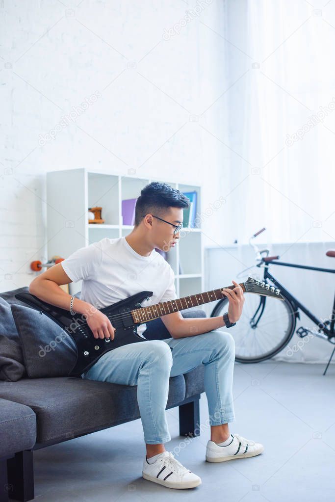 Handsome asian man playing F major chord on unplugged electric guitar at home