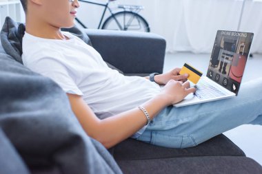online rezervasyon cihaz ile dizüstü bilgisayar kullanarak ve kredi kartı evde kanepenin üzerinde tutan adamın resim kırpılmış