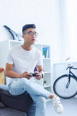 üzgün yakışıklı Asya adam evde kanepenin üzerinde video oyun oynarken