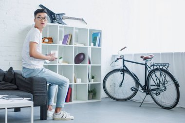 kahve ile kanepe tarafında oturan ve uzağa oturma odasında arıyorsunuz Asya yakışıklı