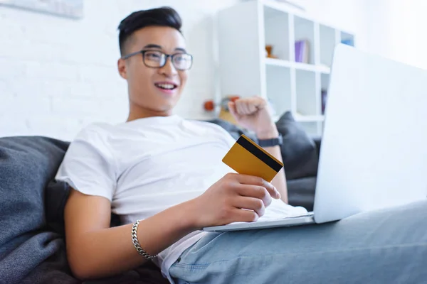 Podekscytowany Przystojny Mężczyzna Azjatyckich Pomocą Laptopa Kanapie Posiadania Karty Kredytowej — Zdjęcie stockowe