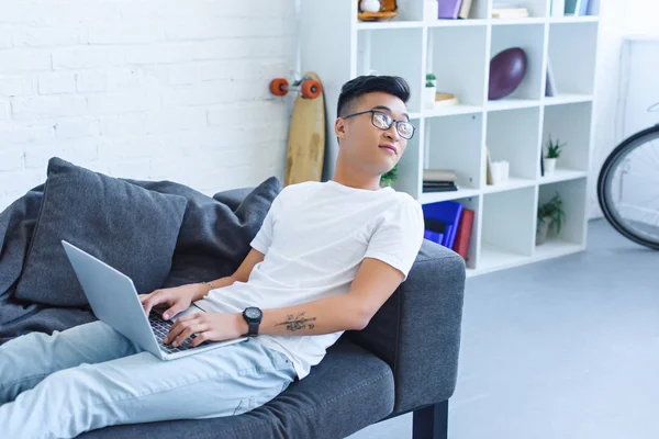 Schöner Asiatischer Mann Benutzt Laptop Auf Sofa Hause Und Schaut — Stockfoto