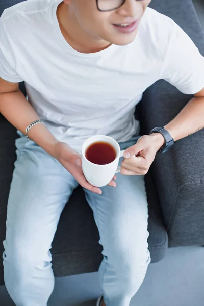 自宅のお茶のカップが付いているソファーに座っている男性の画像をトリミング  — 無料ストックフォト
