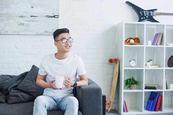 Sonriente Guapo Asiático Hombre Sentado Sofá Con Taza Café Mirando — Foto de Stock