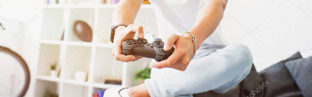 cropped image of man playing video game on sofa and holding gamepad at home