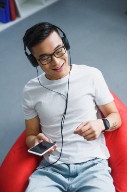 gülümseyen genç adam akıllı telefon kullanarak ve kulaklık müzik yüksek açılı görünüş