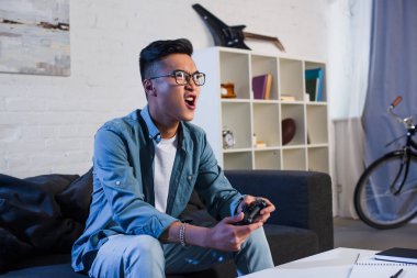 bağırıyor ve evde joystick ile bilgisayar oyunu oynamak heyecanlı Genç Asyalı adam 