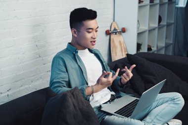kanepede oturan ve orta parmak laptop veren Genç Asyalı adam