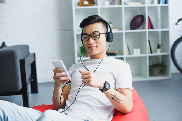 Jovem Asiático Homem Fones Ouvido Usando Smartphone Enquanto Sentado Feijão — Fotografia de Stock