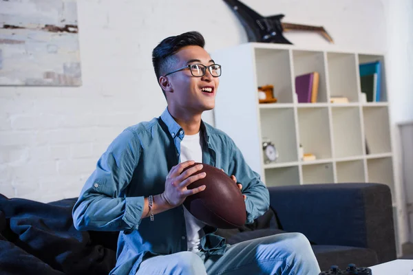 Feliz Joven Asiático Hombre Gafas Celebración Rugby Pelota Viendo Deporte —  Fotos de Stock