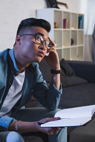 Pensativo Joven Asiático Hombre Gafas Celebración Notebook Mirando Hacia Fuera —  Fotos de Stock