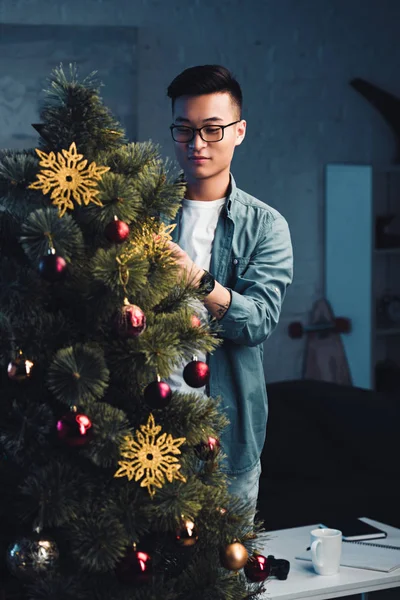 戴眼镜的亚洲年轻人在家装饰圣诞树 — 图库照片