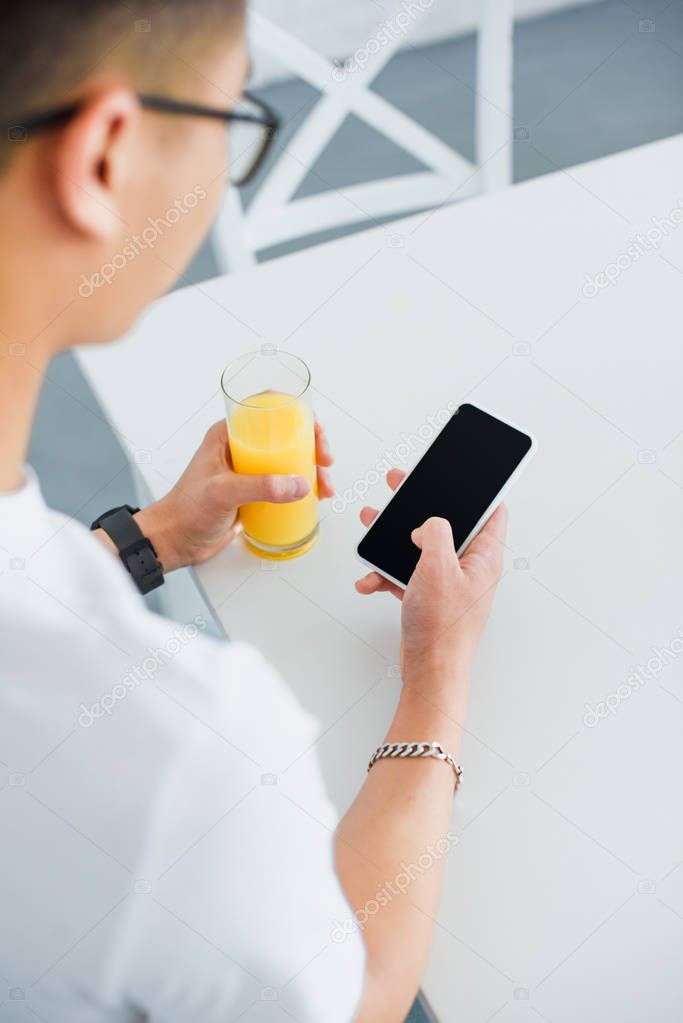 Cropped shot of young man holding glass of juice and using smartphone with blank screen