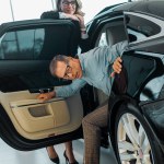 Adult man checking luxury car with female car dealer at showroom