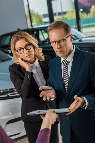 Confused Businesspeople Listening Female Car Dealer Papers Showroom — Stock Photo, Image