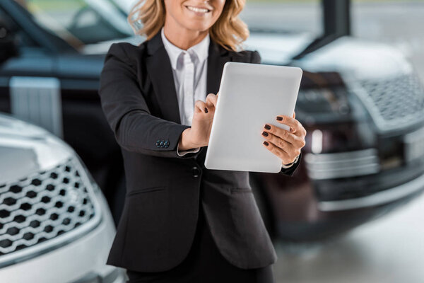 cropped shot of smiling female car dealer holding tablet in showroom